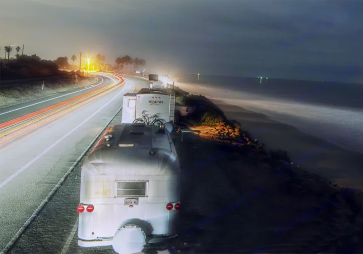 RV rentals and travel trailers parked along a coastal road at night, with long exposure car light trails and ocean waves.. Fleetwood Pulse 2009