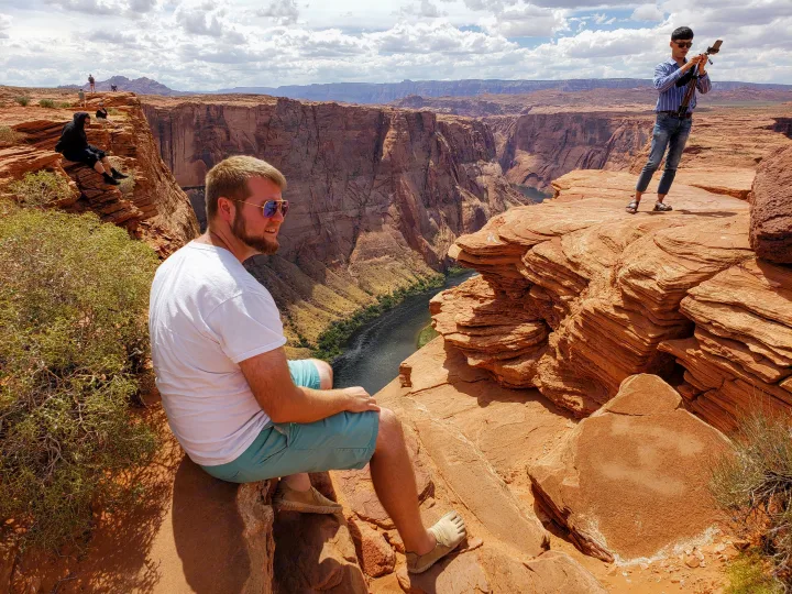 Explore stunning canyon vistas via RV rental! A man relaxes, admiring the vast red rock landscape and winding river below.. Fleetwood Pulse 2009