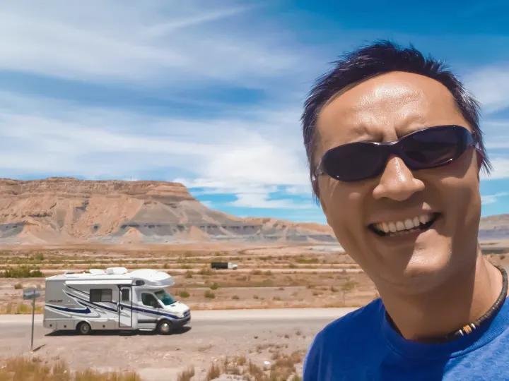 Enjoying an RV rental adventure! A smiling man and his RV on a desert road trip with mountains and blue skies.. Fleetwood Pulse 2009