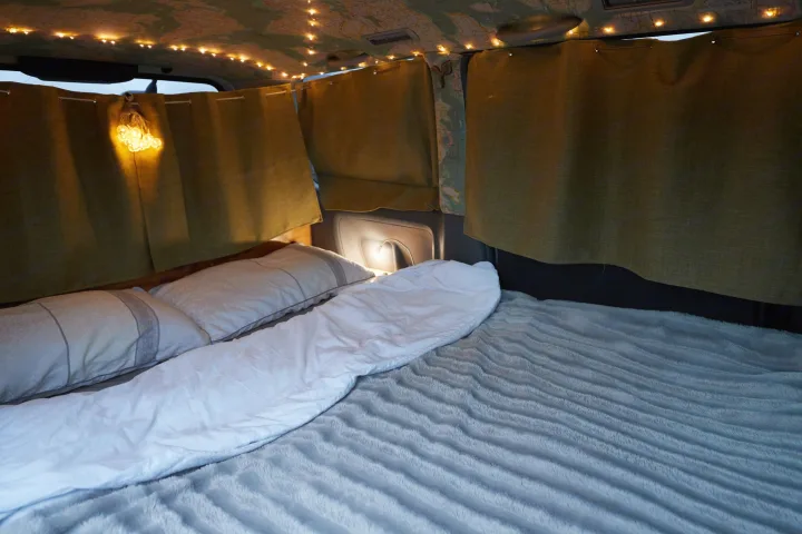 Cozy RV rental interior with comfortable bed, string lights on map ceiling, and olive green privacy curtains.. Toyota Voxy 2007