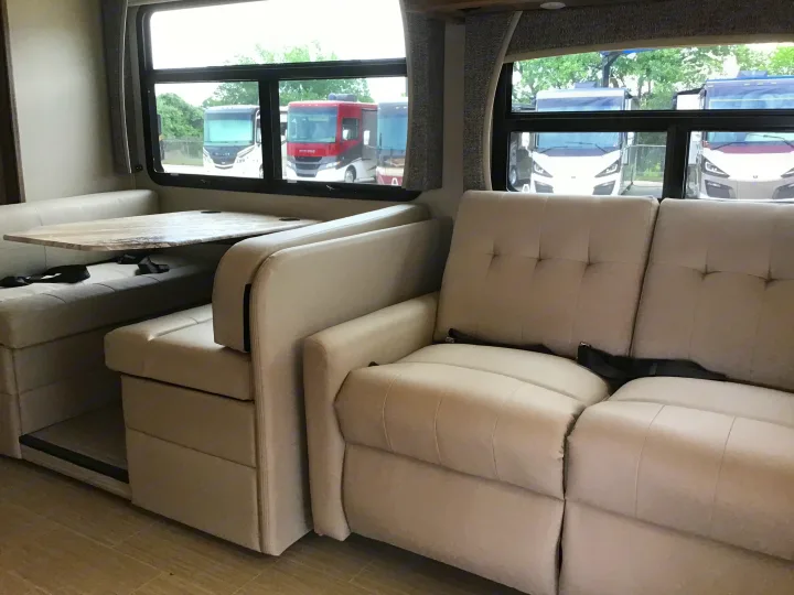 Inside an RV rental, a light-colored dinette and sofa create a welcoming living space, with other RVs visible outside.. Jayco Greyhawk 2022
