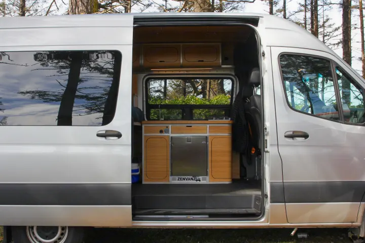 Silver RV rental: open door reveals custom Zenvanz camper interior with kitchenette, fridge, and cabinets. Ready for adventure!. Mercedes-Benz Sprinter 2018