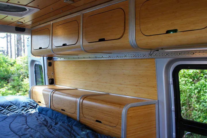An RV rental interior with sleek bamboo cabinets, bed, and wall panels, offering a cozy mobile living space.. Mercedes-Benz Sprinter 2018