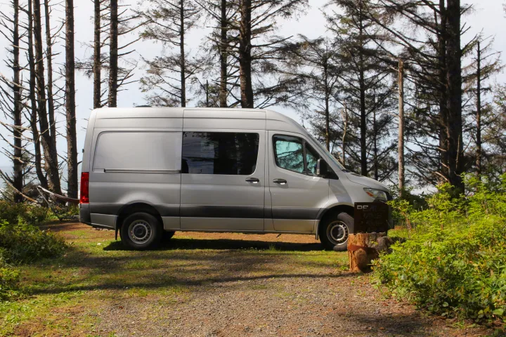 Silver Sprinter camper van parked among coastal trees at a 'Peace Vans Camp' site, perfect for RV rental adventures.. Mercedes-Benz Sprinter 2018