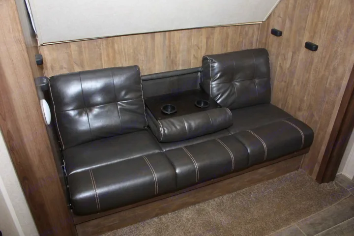 Inside an RV rental: Dark tufted RV bunk sofa with a central armrest featuring two cup holders, offering comfortable seating.. Palomino Puma 2018