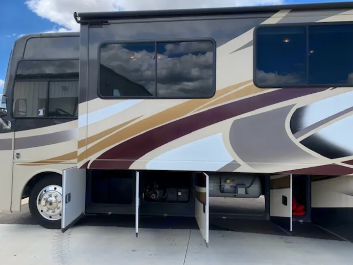 RV rental motorhome, side view. Its multi-colored exterior has open storage bays showing various equipment.. Thor Motor Coach Miramar 2014