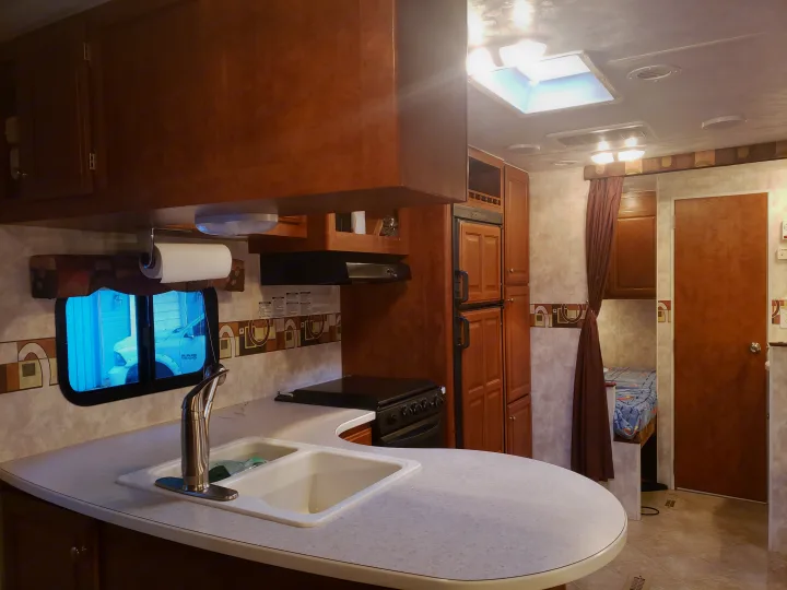 Explore this RV rental's well-equipped kitchen featuring a sink, stove, fridge, and ample wooden cabinetry in a cozy travel trailer.. Pacific Coachworks Tango 2010