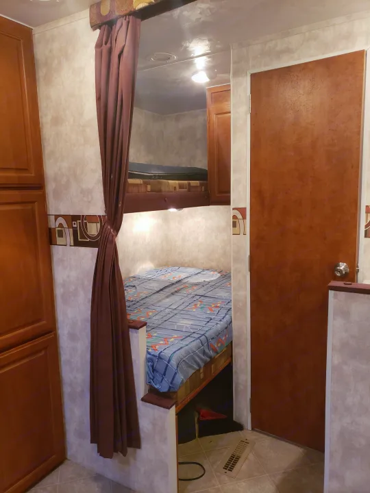 RV rental interior: Bunk beds with a tied-back privacy curtain, wooden cabinetry, and a door to a compact sleeping area.. Pacific Coachworks Tango 2010