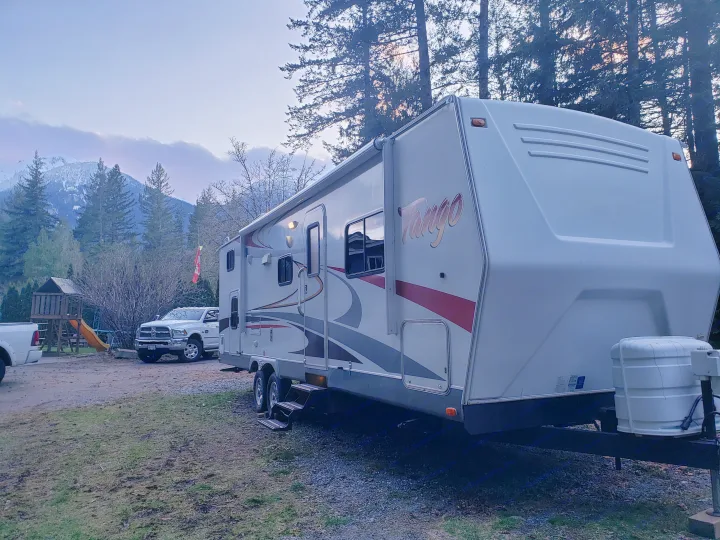 Enjoy your RV rental vacation! A white Tango travel trailer sits by snow-capped mountains, trees & a truck at dusk.. Pacific Coachworks Tango 2010