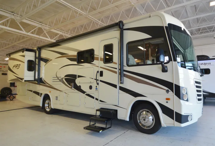 Large, modern white RV with black & brown graphics, featuring a slide-out extension, displayed indoors. Ideal for rv rental.. Forest River Fr3 2019