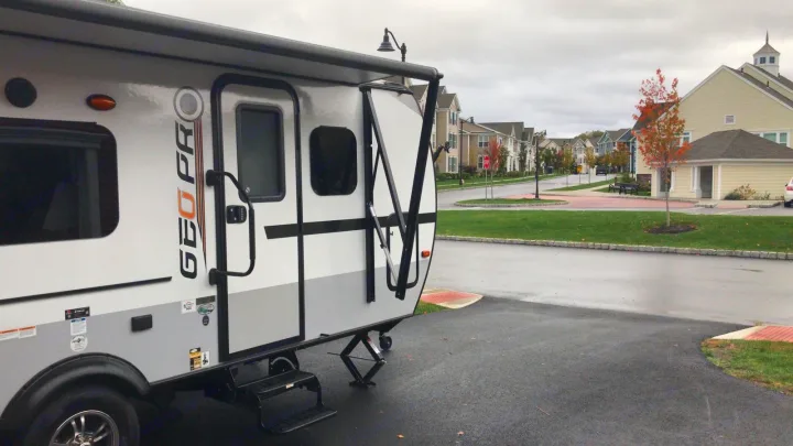 White and gray Geo Pro RV rental, parked with awning out, in a residential development.. Forest River Rockwood 2018