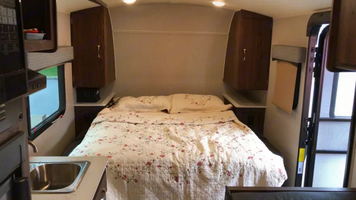 Cozy RV rental interior featuring a bed with a floral quilt, overhead cabinets, and a compact kitchen sink area.. Forest River Rockwood 2018