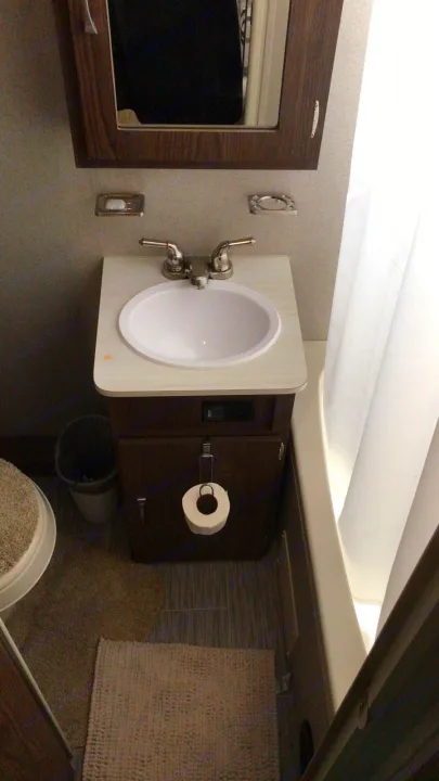 Compact RV rental bathroom: vanity with sink & TP holder, medicine cabinet, tub with curtain.. Forest River Rockwood 2018