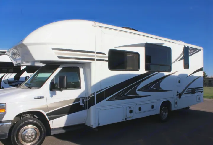 This large, white motorhome rv rental features sleek black and grey decals and multiple windows, parked outdoors.. Jayco Envoy 2018