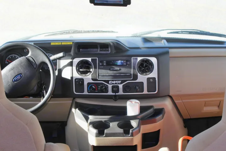 RV rental interior: Ford E-Series dashboard showing steering wheel, radio, climate controls, and passenger console.. Jayco Envoy 2018