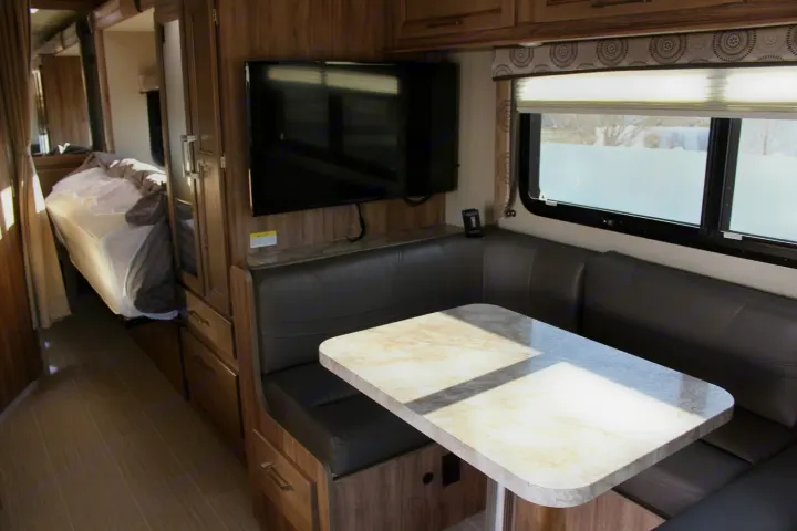This rv rental interior showcases a dining booth, wall-mounted TV, and space-saving fold-down bed.. Entegra Coach Odyssey 24B 2020