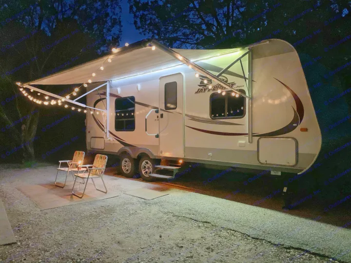 Nighttime scene: A well-lit RV rental with an extended awning, string lights, chairs, and a lantern.. Jayco Jay Flight 2014