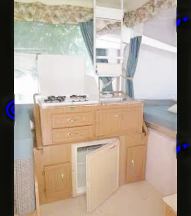 Compact pop-up camper interior with a kitchen (stove, sink, fridge) and bed areas, ready for your rv rental adventure.. Coleman Destiny Cheyenne 1998