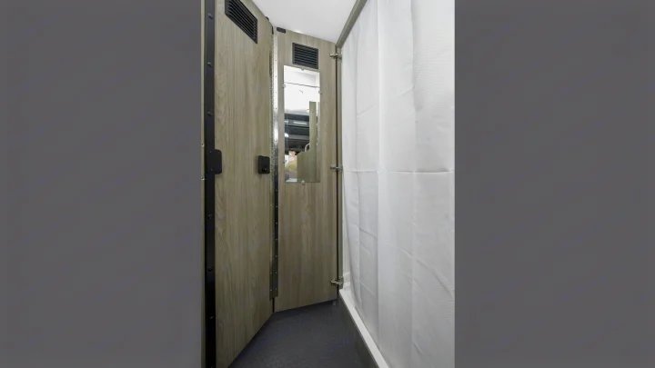Compact RV rental bathroom: a narrow space with a white shower curtain, mirror on a light wood-paneled wall, and patterned floor.. Winnebago Solis 2021