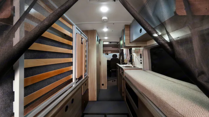 Inside a compact rv rental camper van, showing a kitchen sink, cushioned bench/bed, and convertible slat bed system.. Winnebago Solis 2021