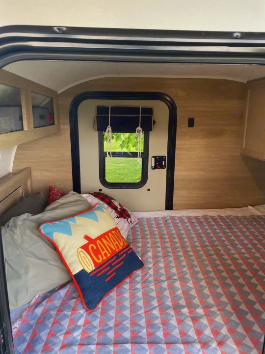 Cozy interior of an RV rental, featuring a bed with a vibrant blanket & Canada pillow, and a view of nature.. Braxton Creek Bushwhacker 2020
