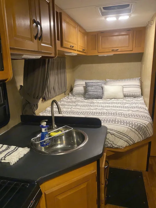 Cozy RV rental interior featuring a bed, kitchen sink, and wood cabinets. Ideal for compact travel.. Thor Motor Coach Four Winds Majestic 2015
