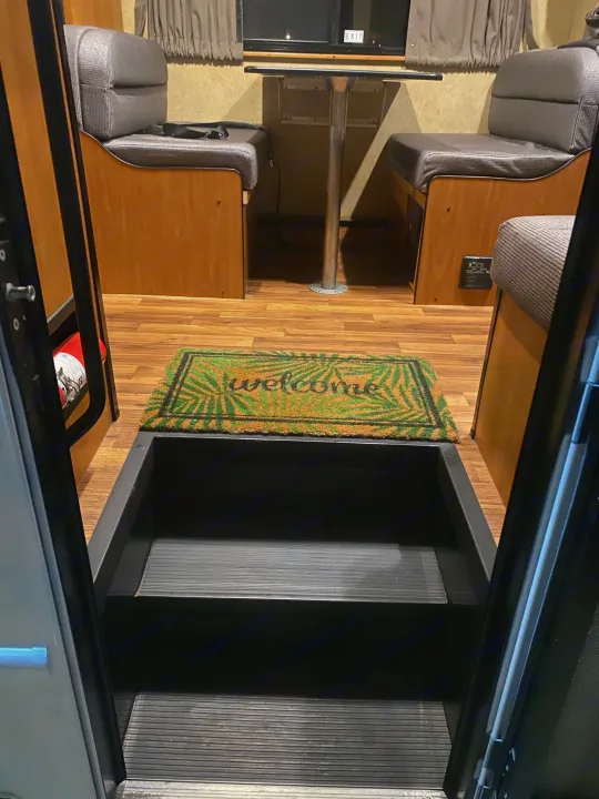 Step inside this cozy RV rental: dinette area with table, seating, and 'Welcome' mat. Fire extinguisher and CO detector visible.. Thor Motor Coach Four Winds Majestic 2015