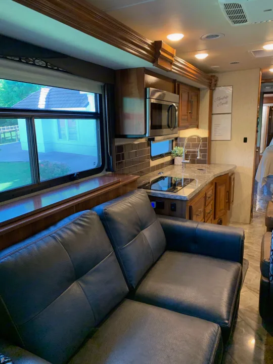 Inside a premium rv rental: Enjoy a sleek kitchen, cozy leather sofa, and large window showcasing the outdoor scenery.. Coachmen Sportscoach 2018