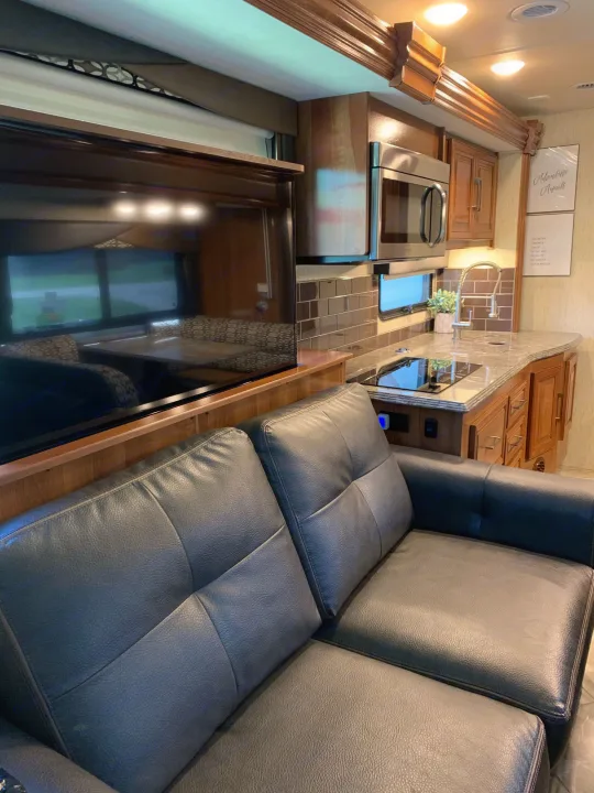 Spacious RV rental interior featuring a comfy black leather sofa, large TV, and full kitchen with a microwave.. Coachmen Sportscoach 2018