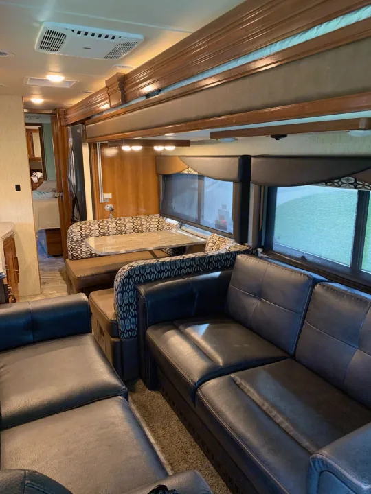 An RV rental's inviting interior with dark faux leather sofas, a patterned dinette, and bright windows.. Coachmen Sportscoach 2018