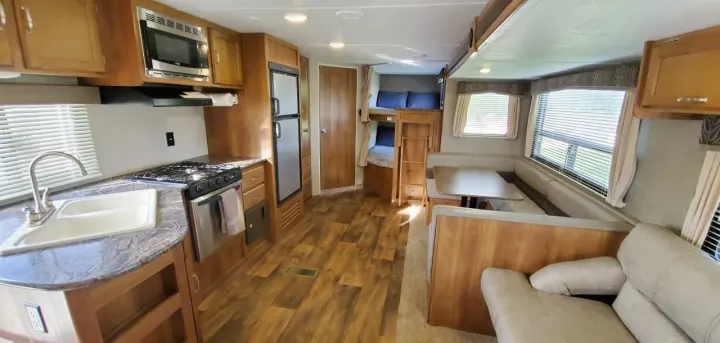 View inside an RV rental: kitchen with stove/sink, dinette, bunk beds, and lounge area, featuring wood cabinetry.. Keystone Springdale 2017