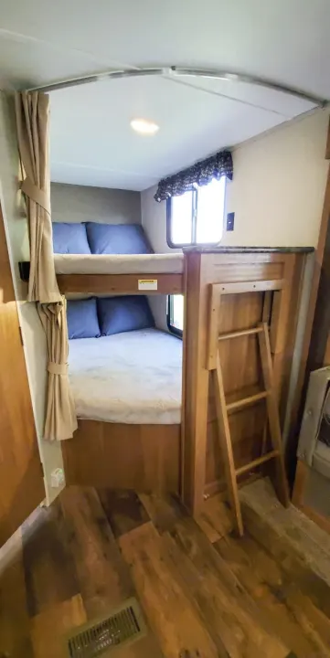 Cozy RV rental interior showing bunk beds with blue pillows, tan curtains, and a ladder for accessing the top bunk.. Keystone Springdale 2017