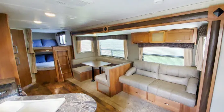 Spacious RV rental interior: bunk beds, U-shaped dinette, and sofa with storage. Windows and cabinets complete the cozy living space.. Keystone Springdale 2017