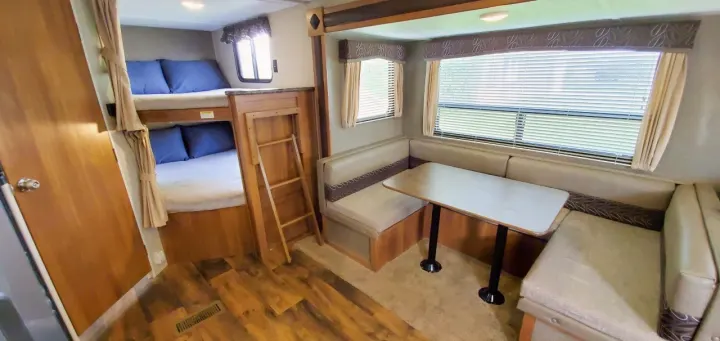 Spacious RV rental interior featuring bunk beds, a U-shaped dinette table, and windows with blinds for comfortable living.. Keystone Springdale 2017