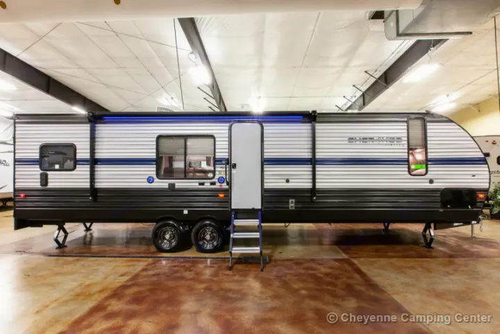 A sleek travel trailer, an ideal RV rental, showcasing a white and black exterior with a blue stripe, open door, and stairs. Ready for adventure.. Forest River Cherokee Grey Wolf 294rr 2020