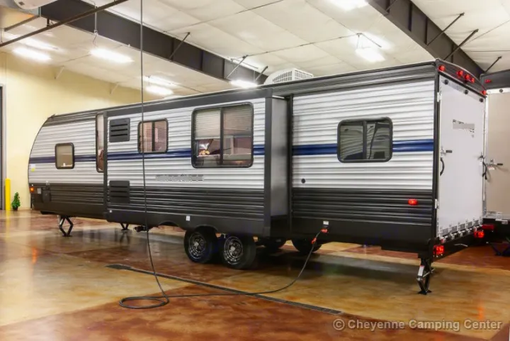 A large, modern travel trailer RV rental with an extended slide-out is showcased indoors, highlighting its spacious design.. Forest River Cherokee Grey Wolf 294rr 2020