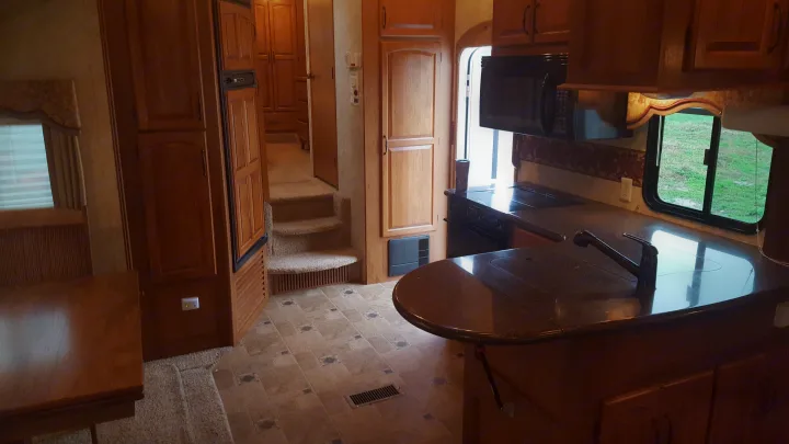 View of an RV rental's living space: a well-equipped kitchen with dining table, counter, sink, and microwave, plus stairs.. Keystone Montana 2011