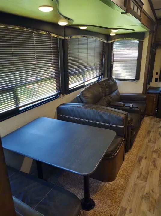 RV rental features a cozy interior: dining booth with table, and a living area with dark leather sofa/recliners & cup holders.. Keystone Cougar 2019