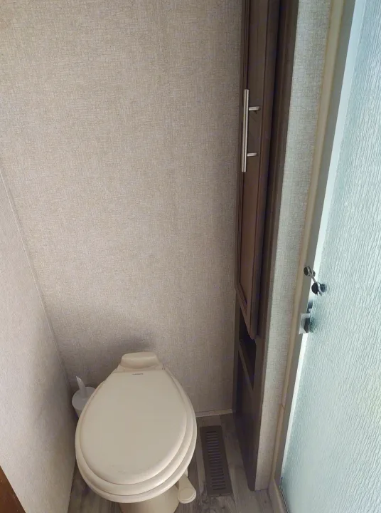 RV rental bathroom interior, showing a toilet, dark wood cabinet, and textured shower door. A compact space.. Keystone Cougar 2019
