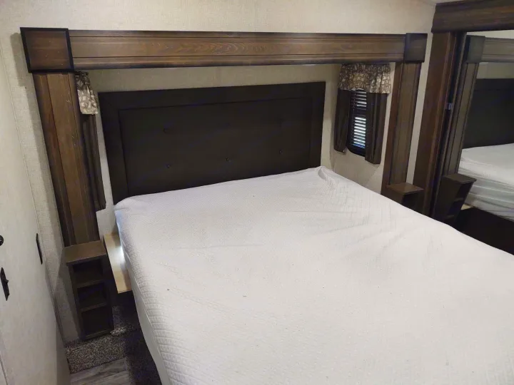 Cozy RV rental bedroom with dark headboard, large bed, framed by wooden accents, featuring small windows and built-in shelves.. Keystone Cougar 2019