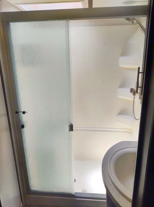 Compact RV rental bathroom: frosted sliding shower door, white tiled walls, built-in shelves, handheld shower, and a small sink.. Keystone Cougar 2019