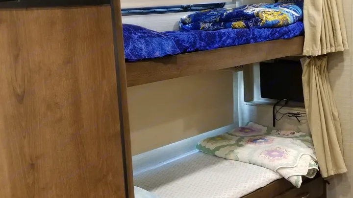 RV rental bunk beds, perfect for family travel. Cozy sleeping area with TV and privacy curtains inside an RV.. Jayco Alante 2018