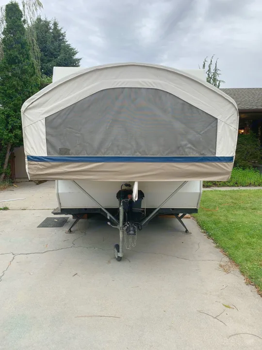 Front of a tan pop-up camper RV rental with a mesh window, parked on a driveway, ready for adventure.. Coachmen Sport 2007