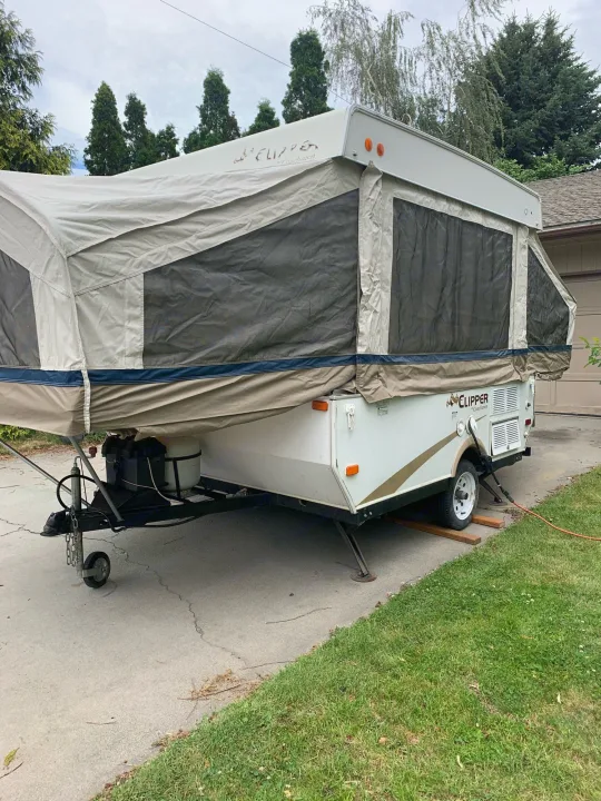 White pop-up camper for RV rental, fully expanded in a driveway, ideal for camping and outdoor adventures.. Coachmen Sport 2007