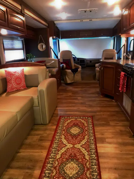 Inside a well-appointed RV rental, a spacious view shows the light-colored sofa, patterned rug, kitchen, and driver's cockpit.. Fleetwood Class A 2015