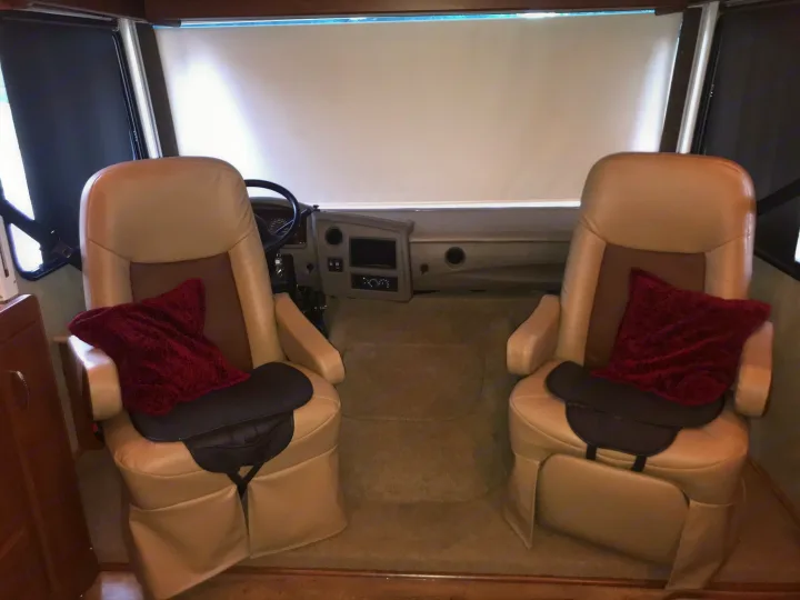 Spacious RV rental driving area with comfortable captain's chairs, ideal for travel. Front windshield covered by shades.. Fleetwood Class A 2015