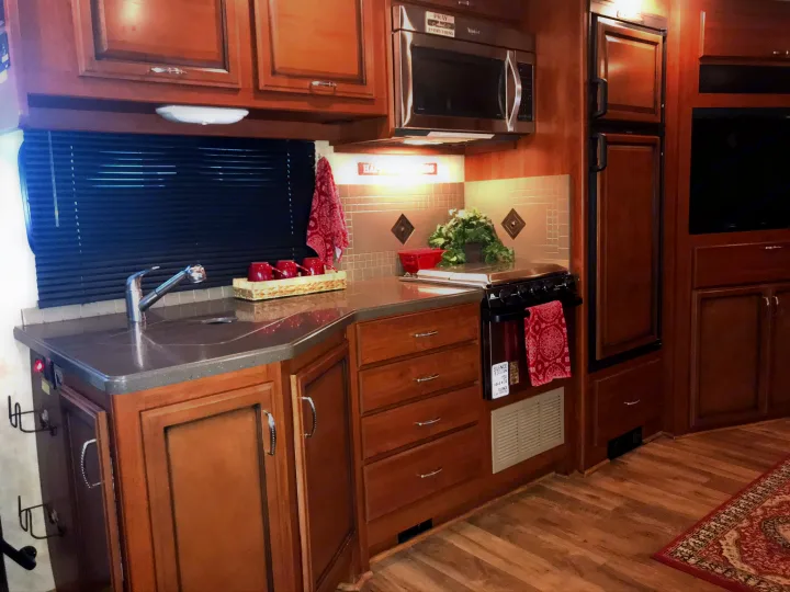 Warm and inviting RV rental kitchen with a sink, microwave, stove, refrigerator, and rich wood cabinets.. Fleetwood Class A 2015