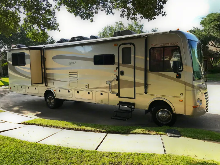 A large Fleetwood Terra Class A motorhome, ready for your next rv rental, is parked on a driveway with its slide-out extended.. Fleetwood Class A 2015