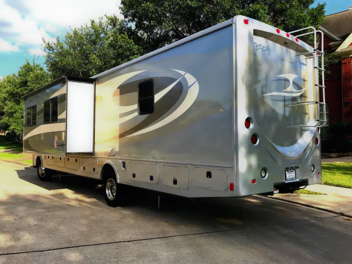 Modern silver motorhome RV rental parked on a driveway with its side slide-out extended for extra space.. Fleetwood Class A 2015