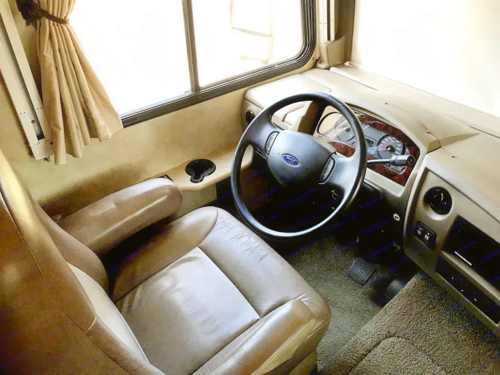 Spacious RV rental driver's cockpit with comfortable tan leather seat, Ford steering wheel, and dashboard. Ready for adventure.. Fleetwood Class A 2015